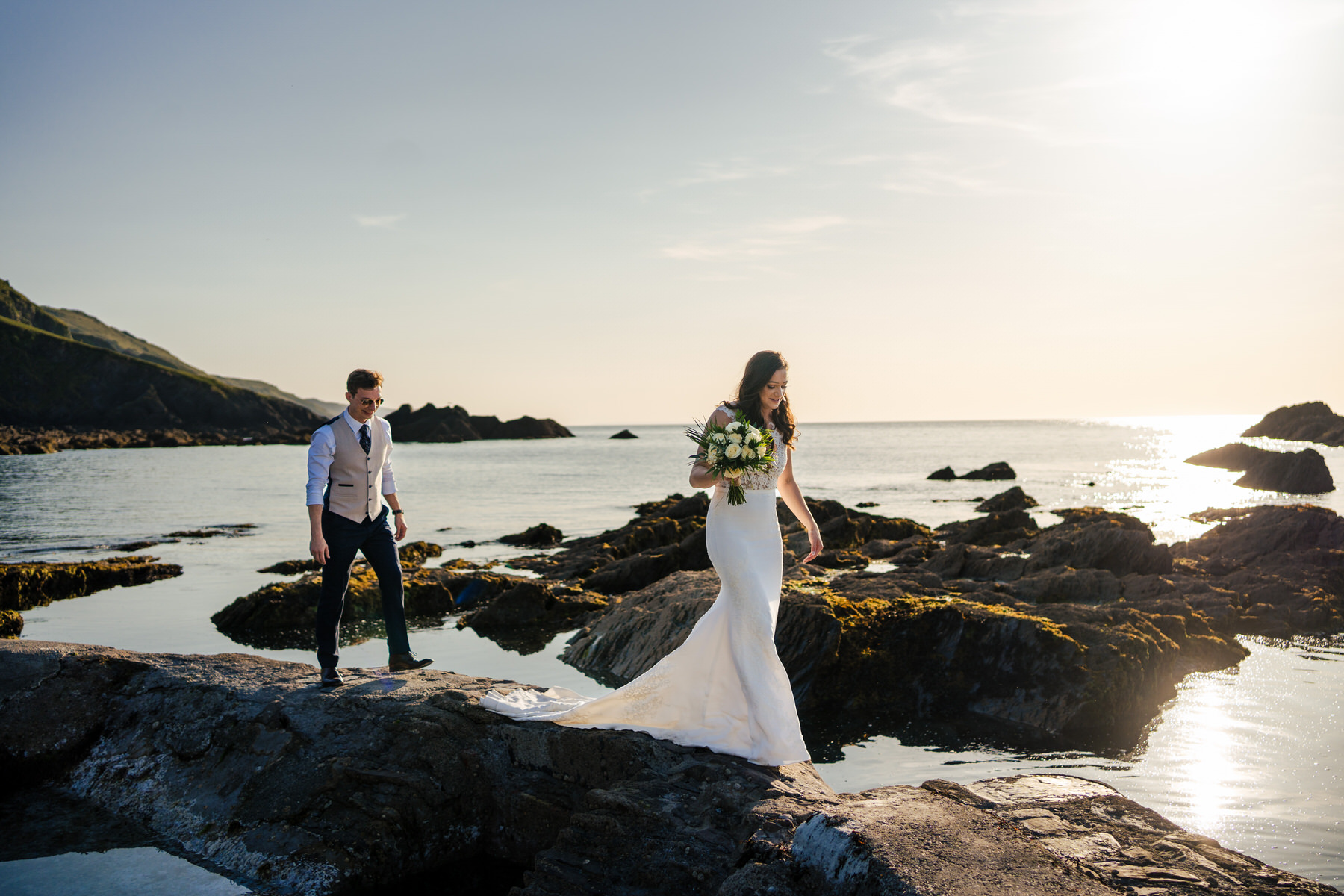A bride and groom kissing in a field at sunset.